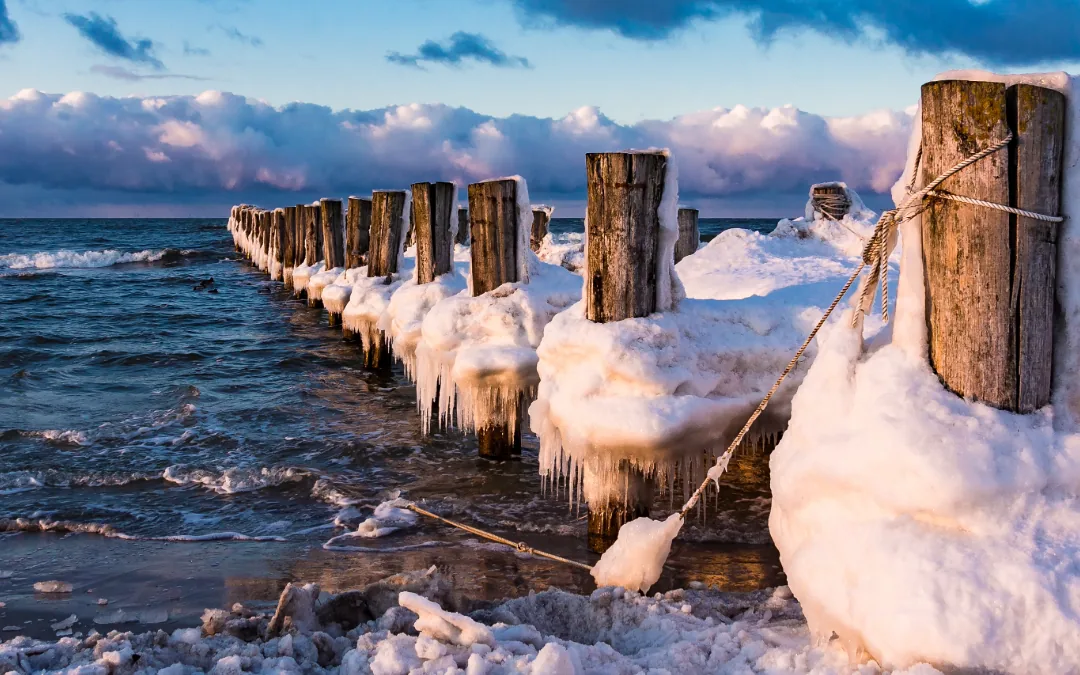 Vereiste Holzbuhnen mit Schnee am Ostseestrand bei Sonnenuntergang